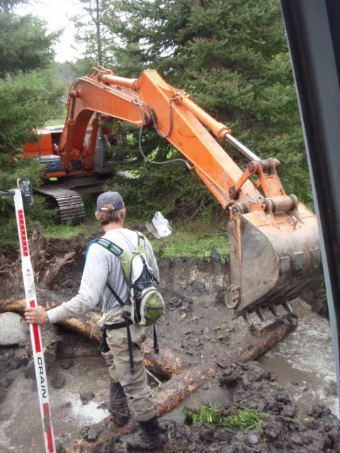 Operator checking grade beside an excavator on a restoration site